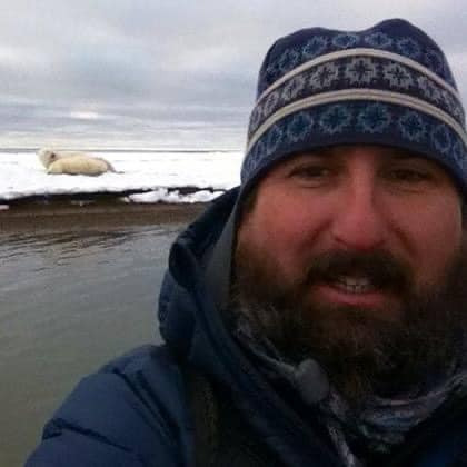 Person in winter clothing with a snowy background and distant polar bear.