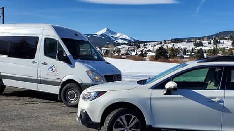 Two vehicles parked with snowy mountains and clear blue sky in background.